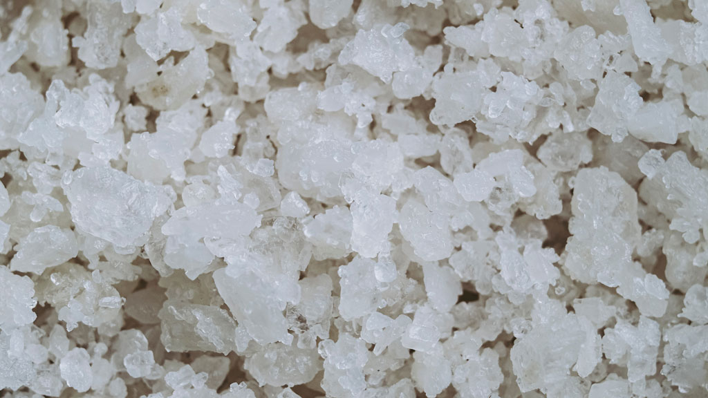 Carafe à décanter en cours de nettoyage avec eau et gros sel visible à l'intérieur, mains tenant la base partiellement visibles